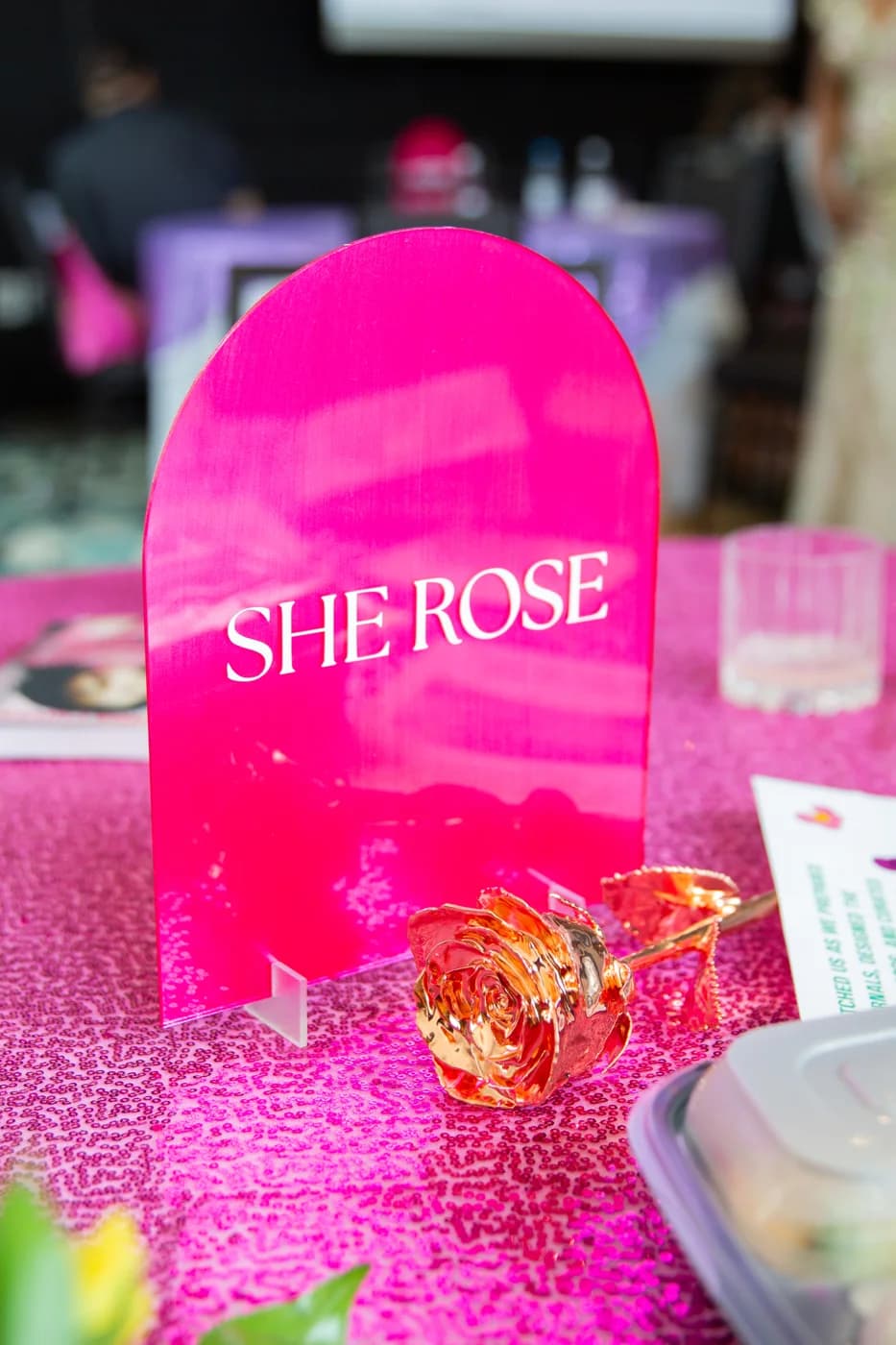 A pink acrylic table sign, shimmering runner, and golden rose detail